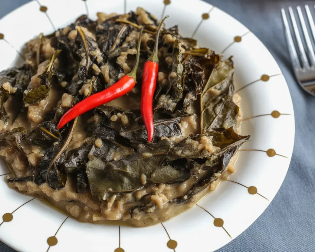A bowl of Laing, featuring dried taro leaves in creamy coconut milk, garnished with chili.