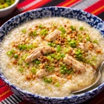 Bowl of creamy Filipino chicken lugaw garnished with green onions and fried garlic.
