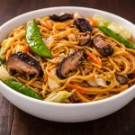 Bowl of easy vegetable pancit canton topped with fresh vegetables and soy sauce.