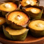 Mini Bibingka Muffins: A Sweet and Simple Filipino Treat 5 Mini bibingka muffins baked in banana leaf-lined tins, topped with cheese and salted egg.